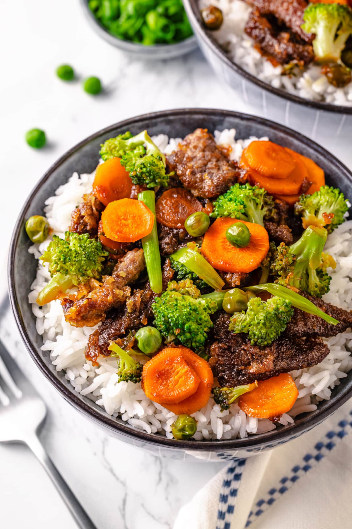 cooked beef with mixed vegetables on white rice in a bowl.