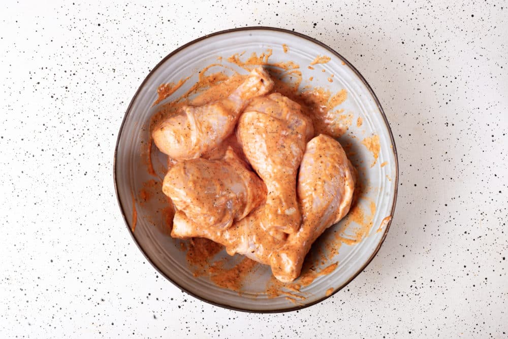 raw chicken legs in a seasoning marinade in a grey bowl with a brown rim.