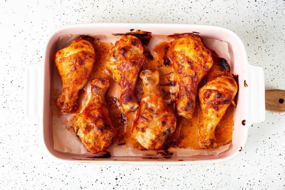 baked spiced chicken legs in a baking dish with parchment paper.