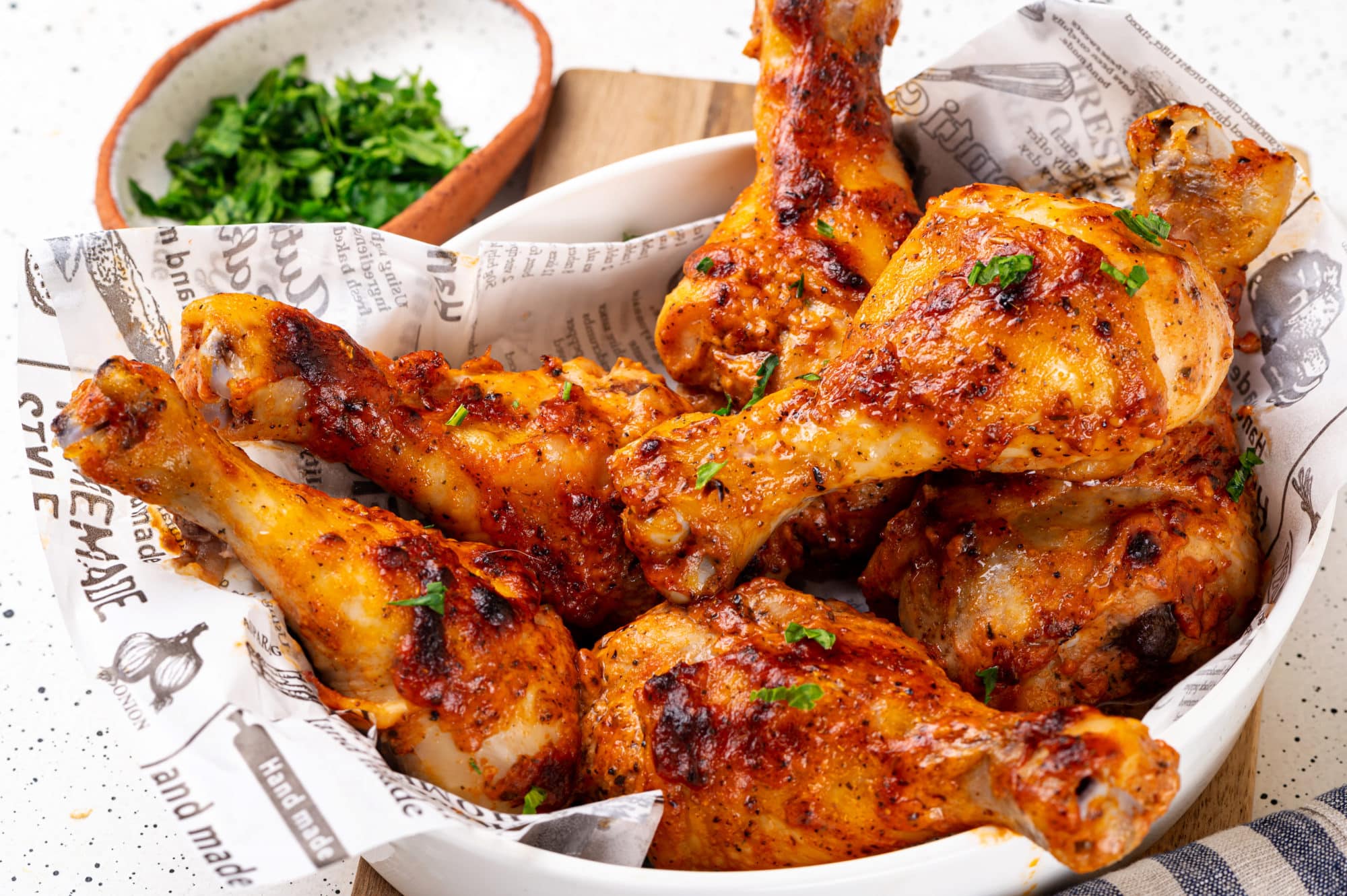 baked chicken in a white dish with paper on a wooden board with a bowl of parsley in the background.