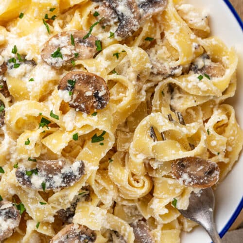 Mushroom alfredo with pasta and extra parmesan, serving on a plate with chopped parsley on top and a fork on the side.