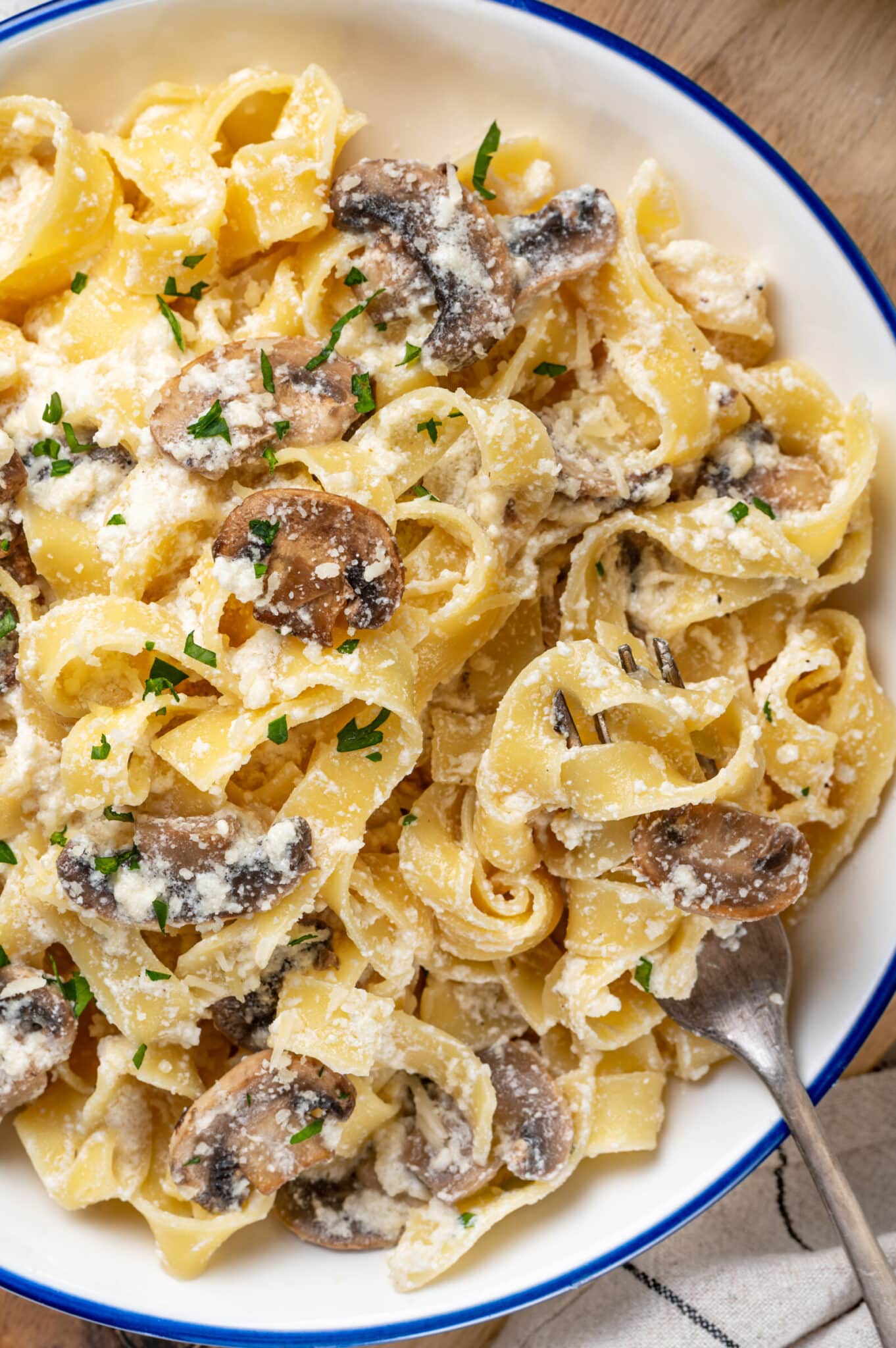 Mushroom alfredo with pasta and extra parmesan, serving on a plate with chopped parsley on top and a fork on the side.