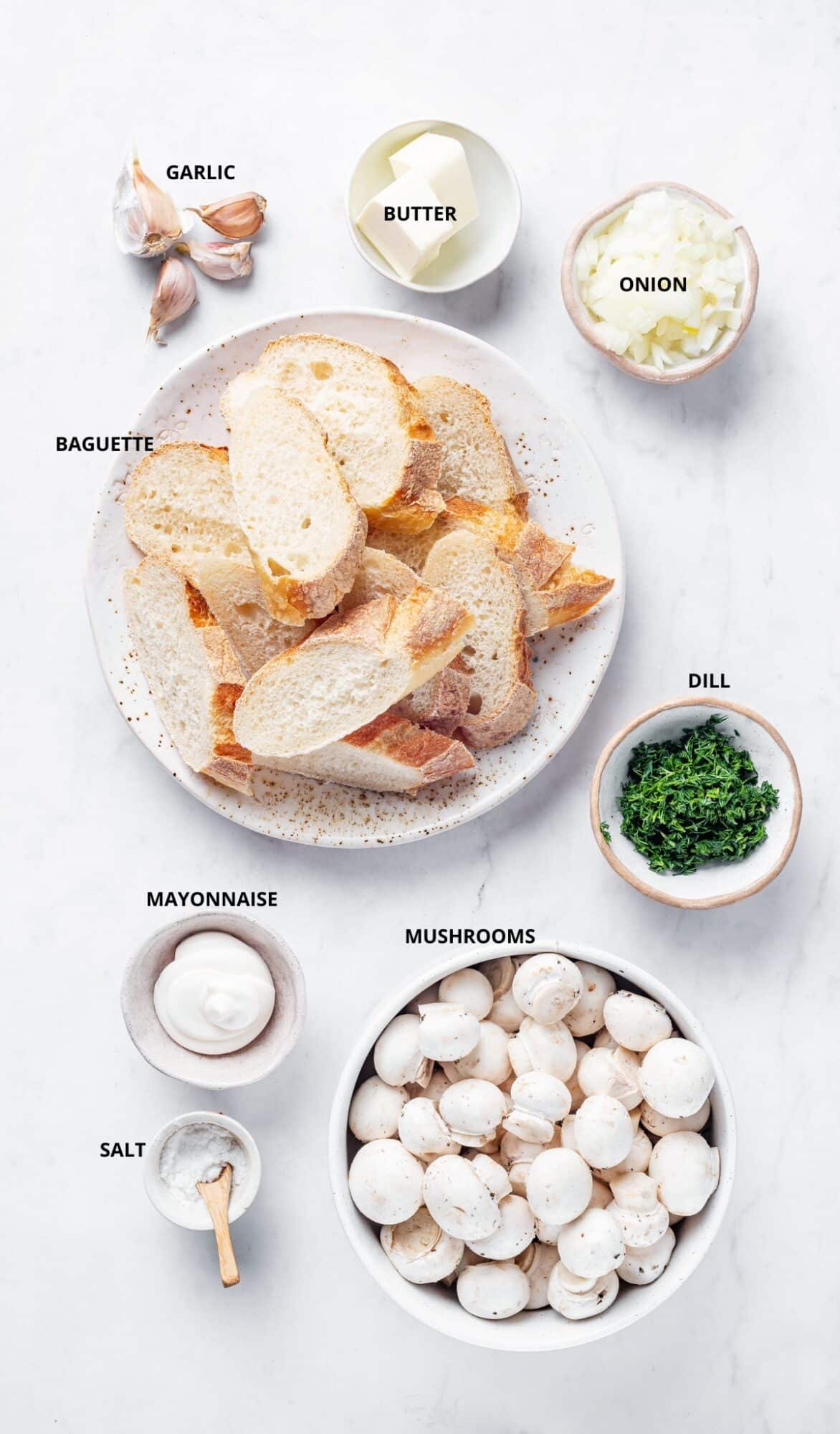 Mushroom crostini ingredients, labeled - mushrooms, baguette, mayonnaise, onion, dill, salt, garlic, and butter.