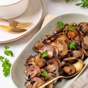 Mushroom side dish in a small white plate with a gold spoon.