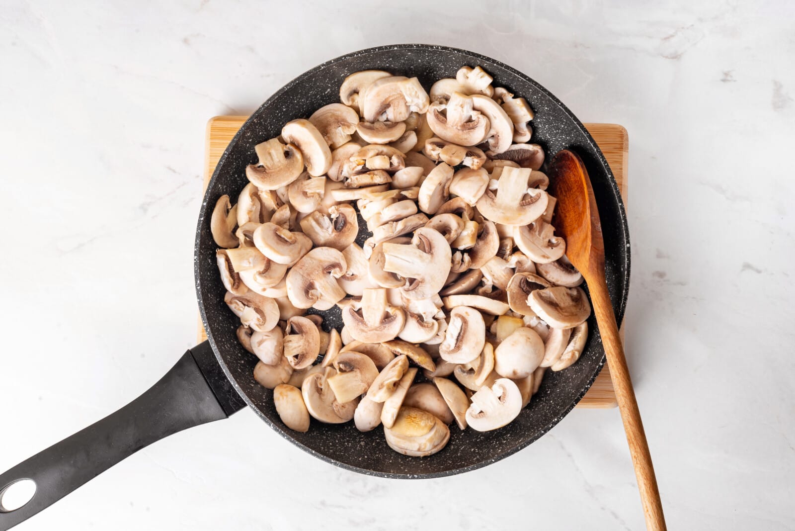 Mushrooms in a skillet with a wooden spoon.