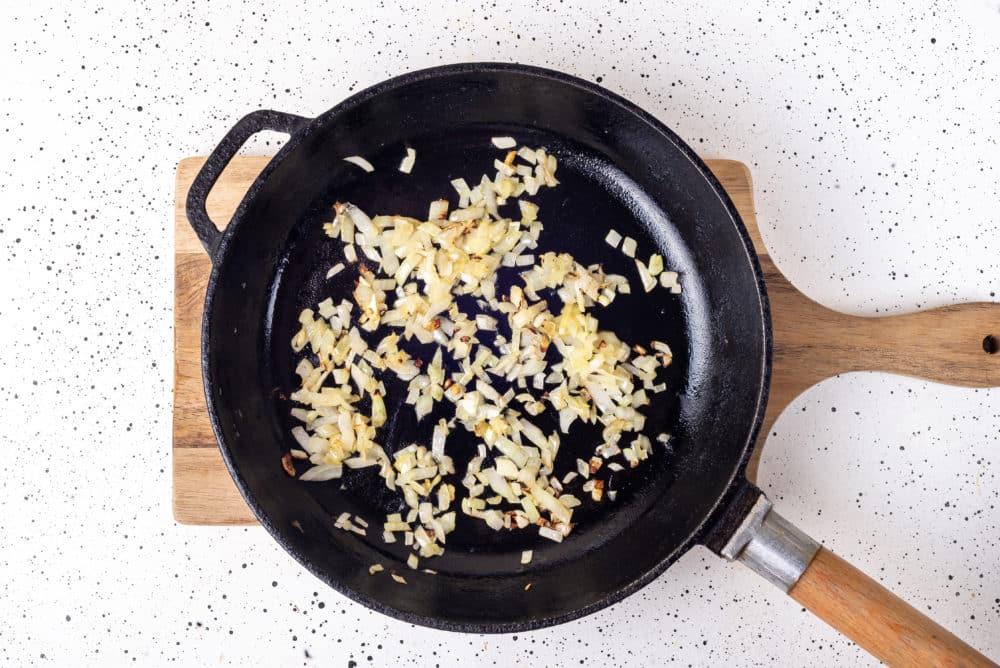 a black skillet on a board with onion sauteeing in it.