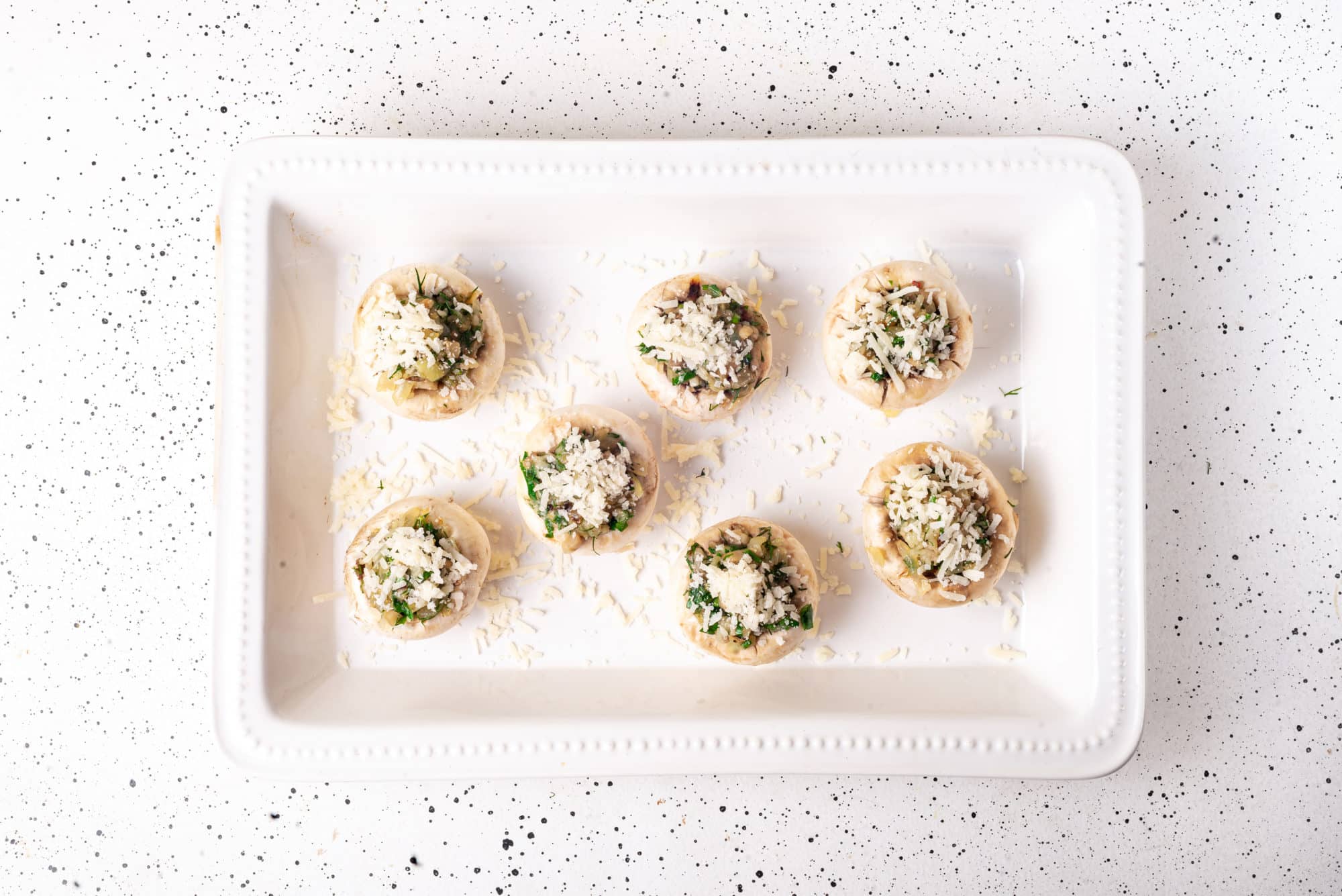 a white dish with ready to bake stuffed mushrooms in it.