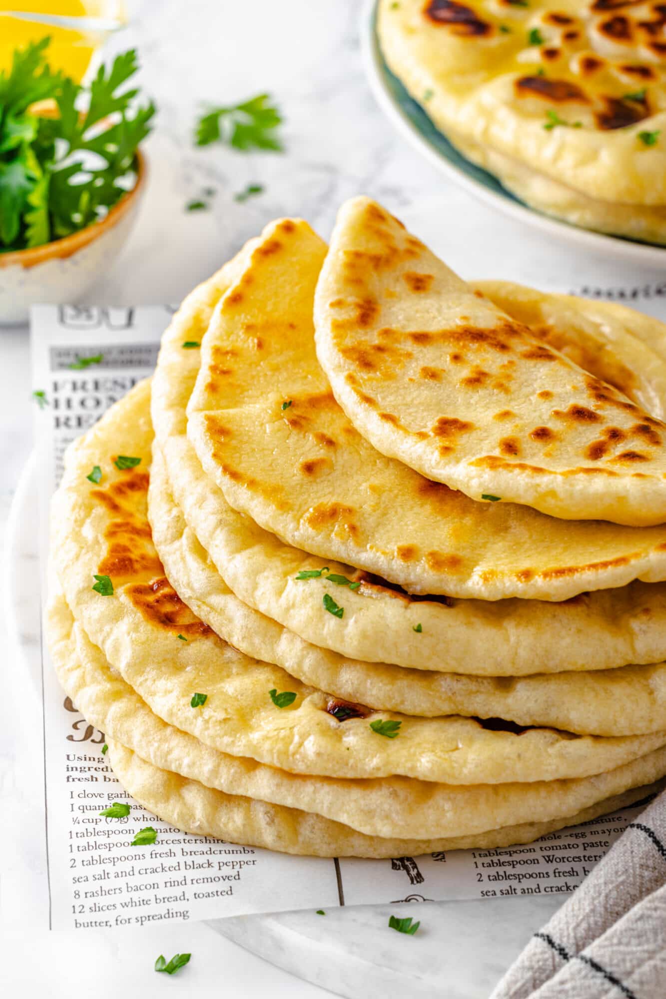 a stack of naan bread with the top couple pieces folded all on top of a newspaper-like recipe sheet.