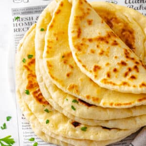 naan bread placed in a stack with the top one folded over on itself and parsley and butter half out of the frame in the top two corners