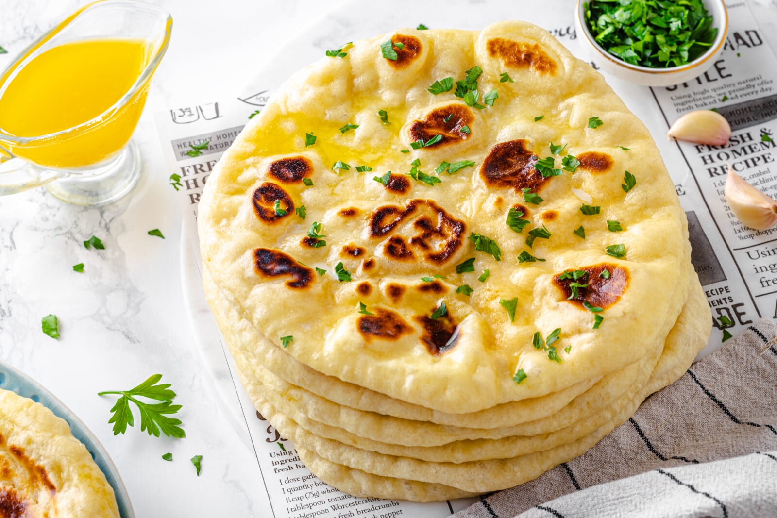 a stack of naan bread on a newspaper with garlic, parsley, and melted butter around it