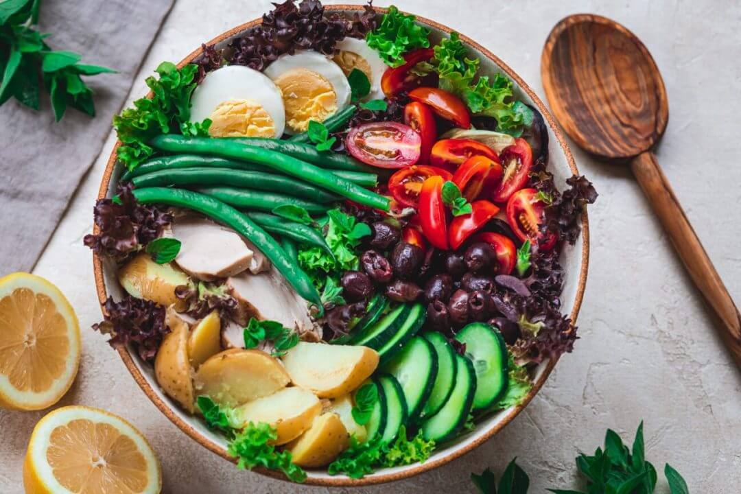 nicoise-salad-in-a-bowl-with-a-wooden-spoon-on-the-side-and-lemon-wedges