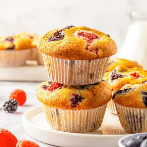 A stack of two no mixer fruit muffins on a white plate surrounded by fresh berries.