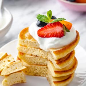 oladky ukrainian pancakes with cream and fresh fruit on top. a section of pancakes are cut out and some are speared on a fork