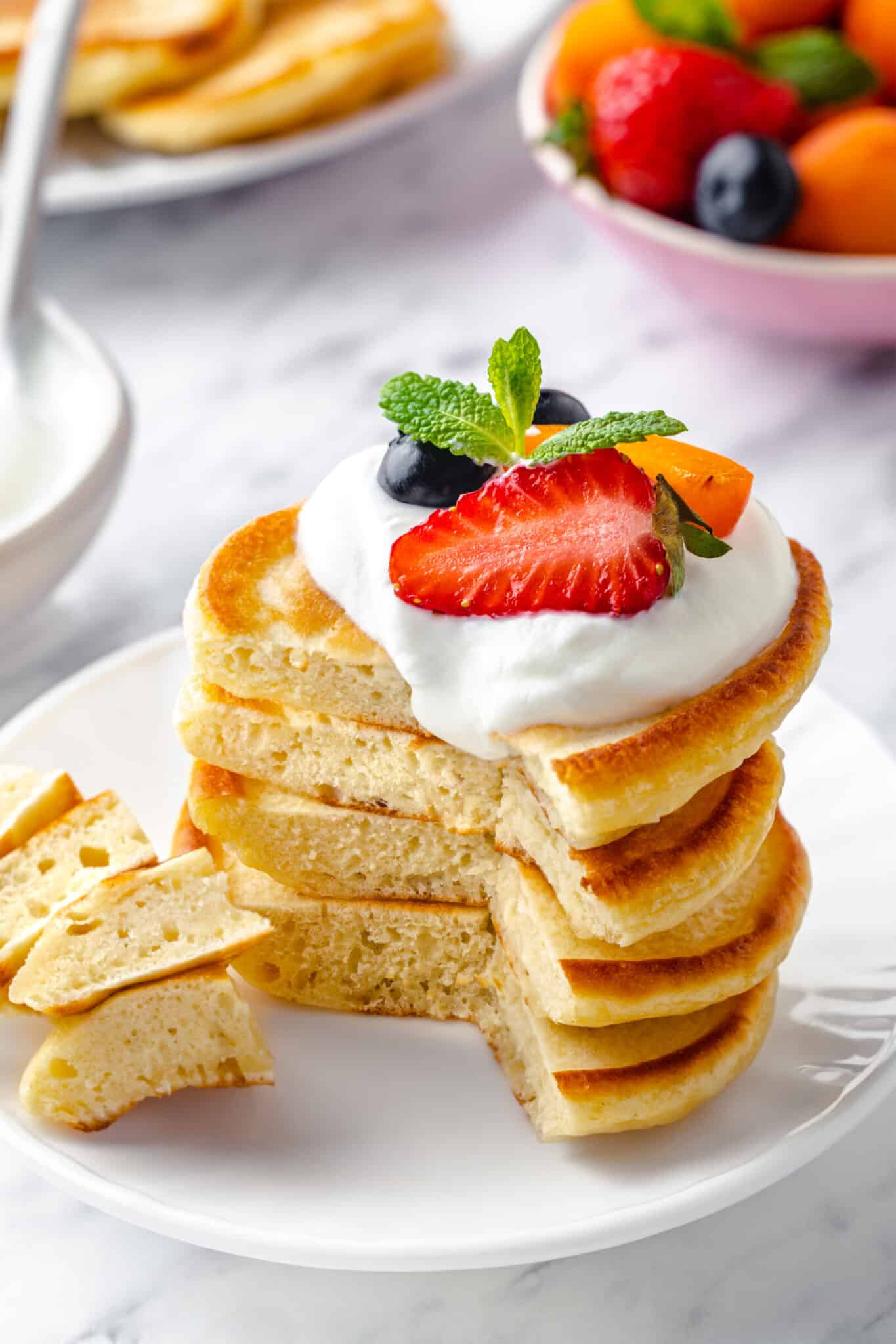 a stake of ukrainian pancakes with a dollop of cream on top and fruit on top of that with a wedge sliced out of it 