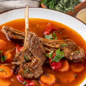 lamb soup with lamb chops on top in a white bowl with a red rim.