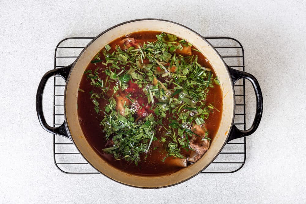 fresh herbs chopped in tomato paste water with lamb chops inside a big black cast iron.