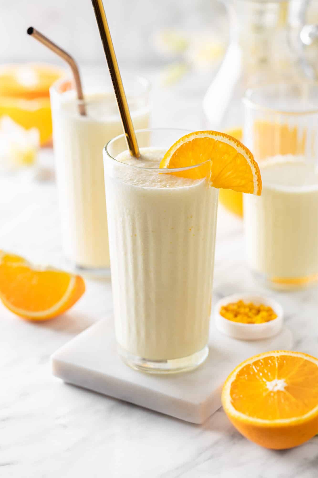 Orange creamsicle smoothie in a glass with a straw on a white board for serving.