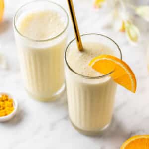 Orange smoothie with creamsicle flavors in glasses with orange zest on the side and an orange slice on the rim.