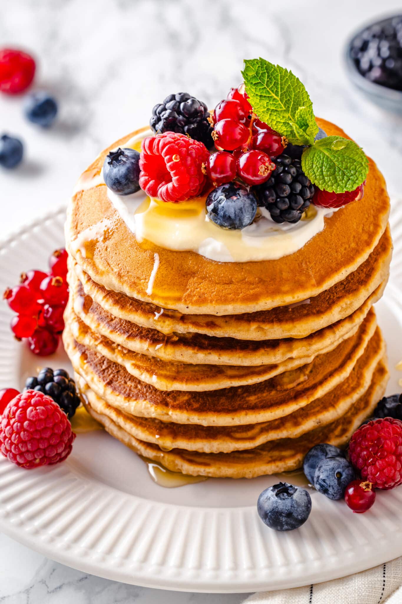 stacked fluffy pancakes with berries on top and mint.