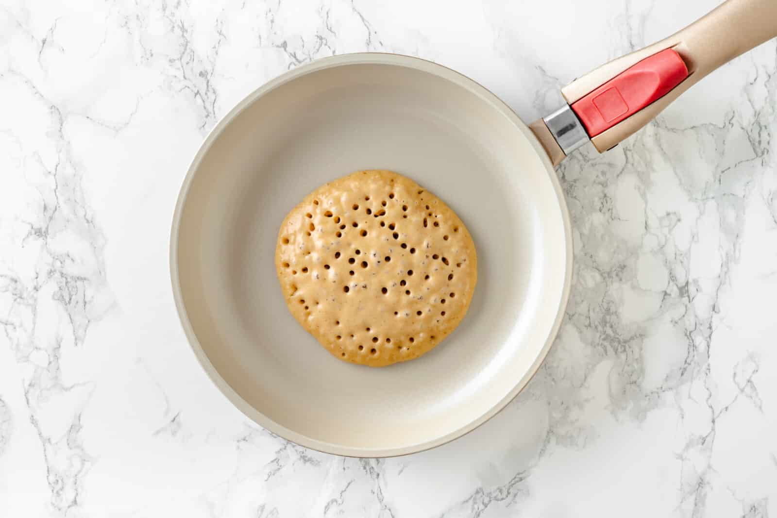 pancake cooking on a skillet with holes in it from the air bubbles