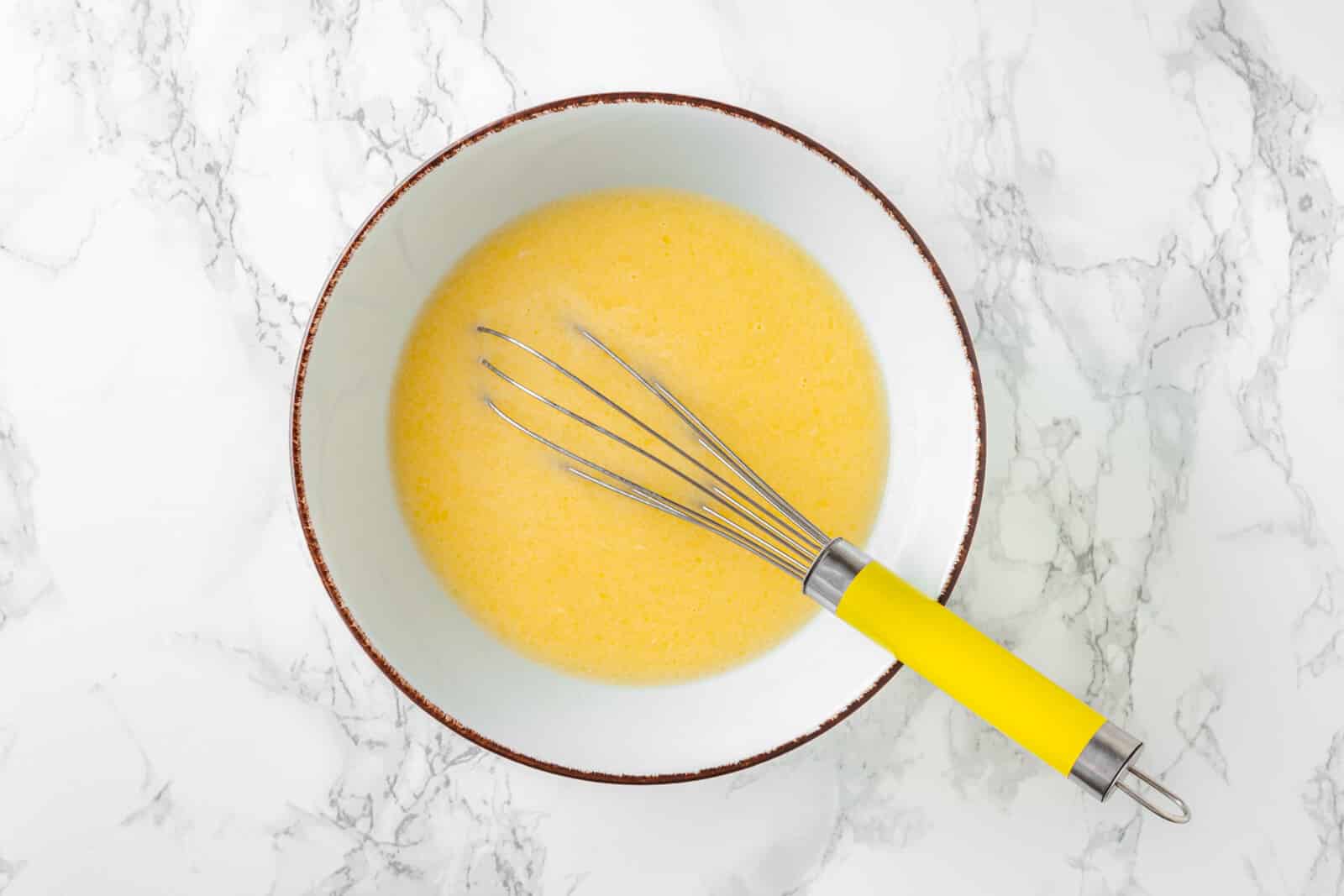 bowl full of an egg and butter mixture with a yellow whisk resting inside