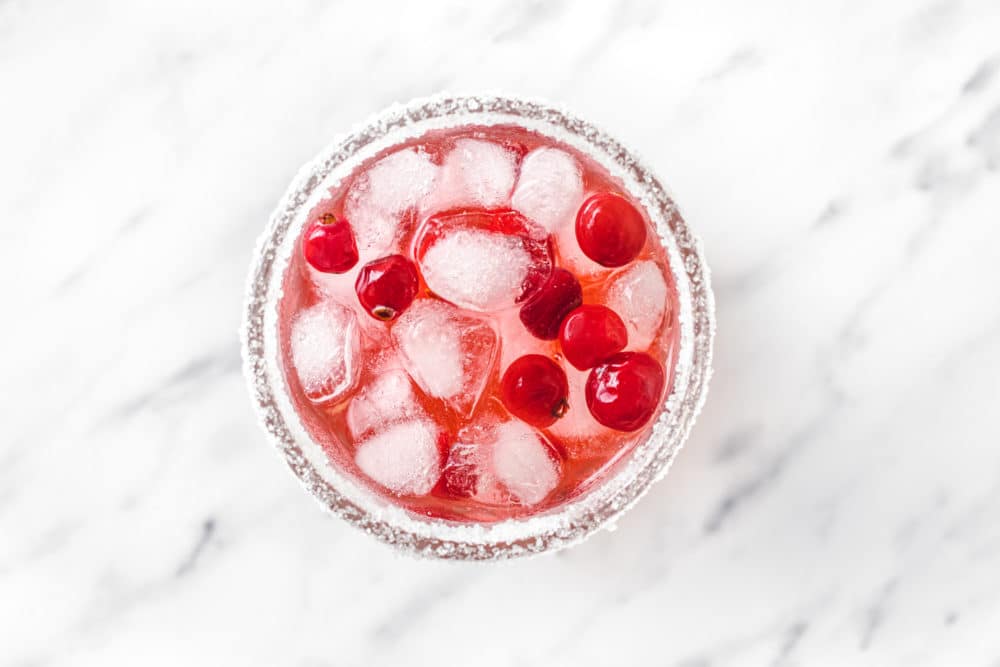 peppermint mocktail being put together in a glass cup with sugar on the rim and cranberries and ice in the drink.