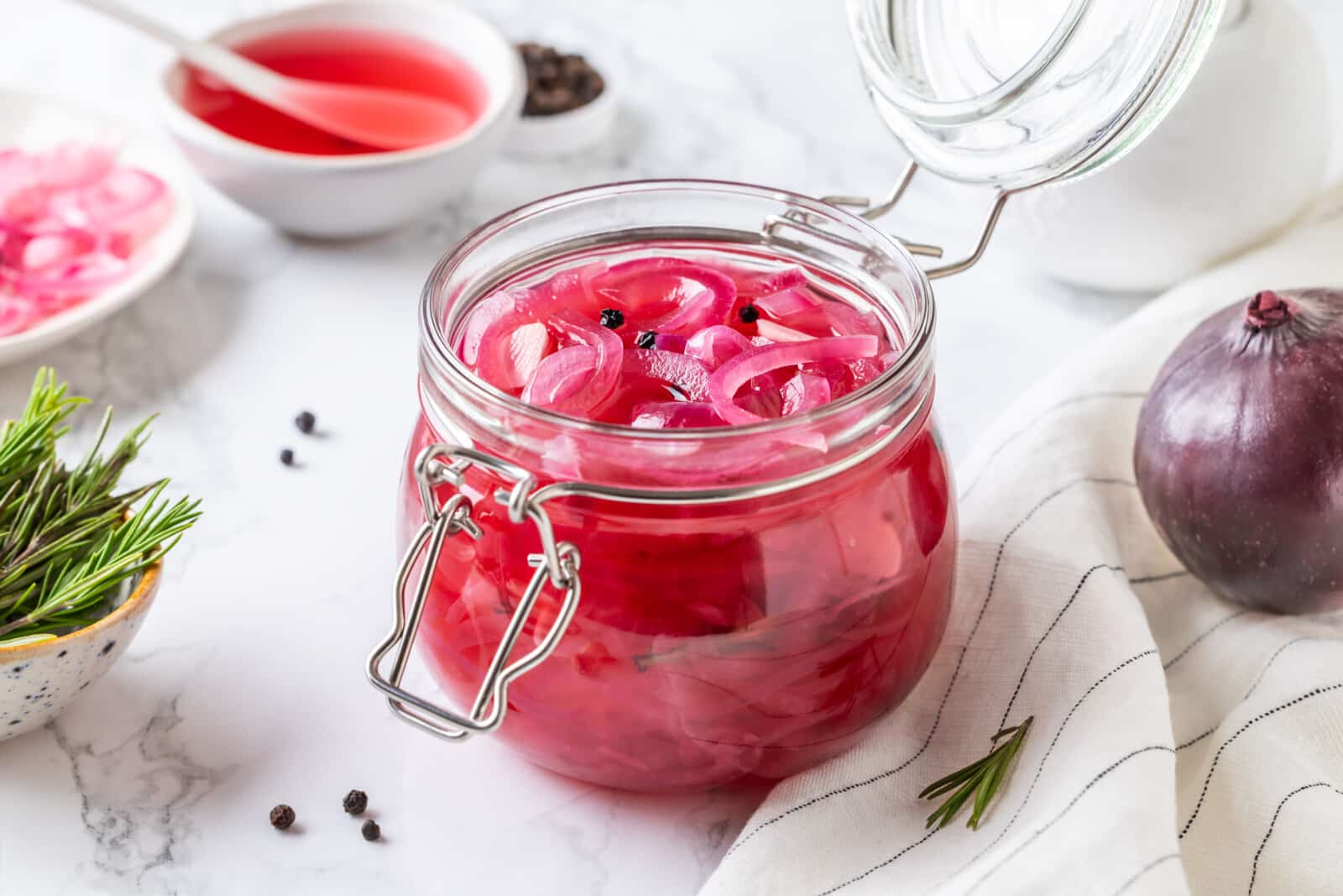 Pickled onion with pickling liquid in a glass jar with ingredients on the side.