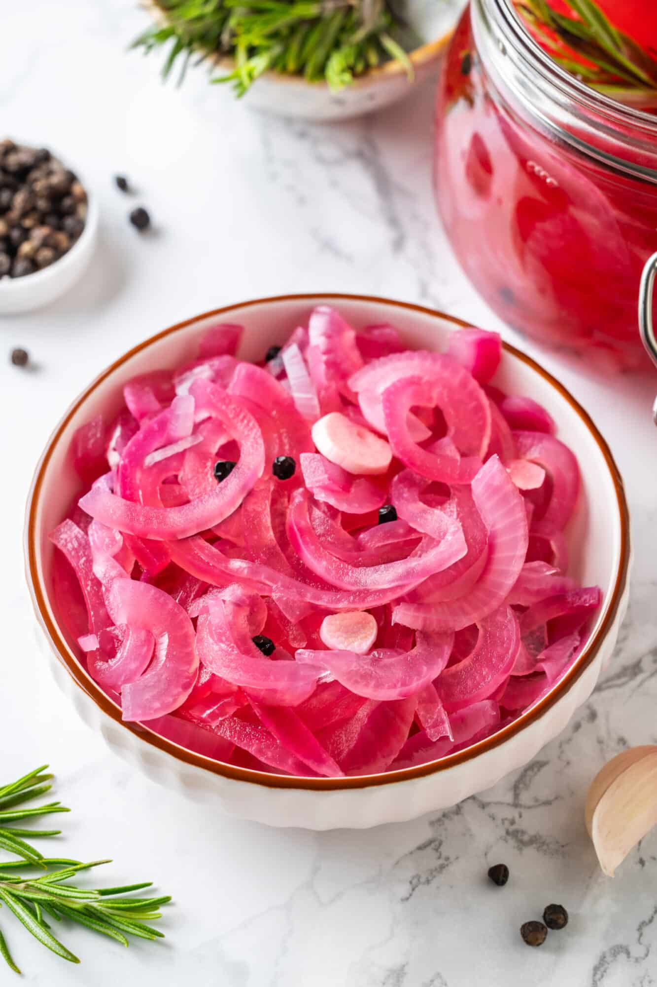 Pickled onions in a white bowl with peppercorns.