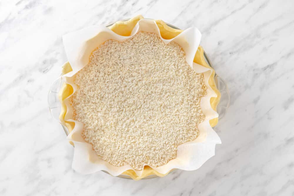 Pumpkin pie crust in a glass dish with rice in as pie weights.