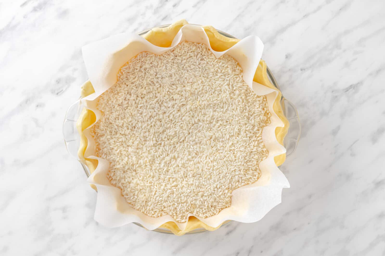 Pumpkin pie crust in a glass dish with rice in as pie weights.