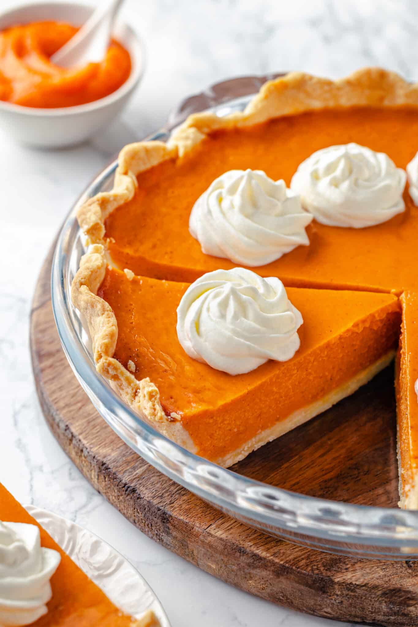 Pumpkin pie in a glass dish with whipped cream dollops on top.