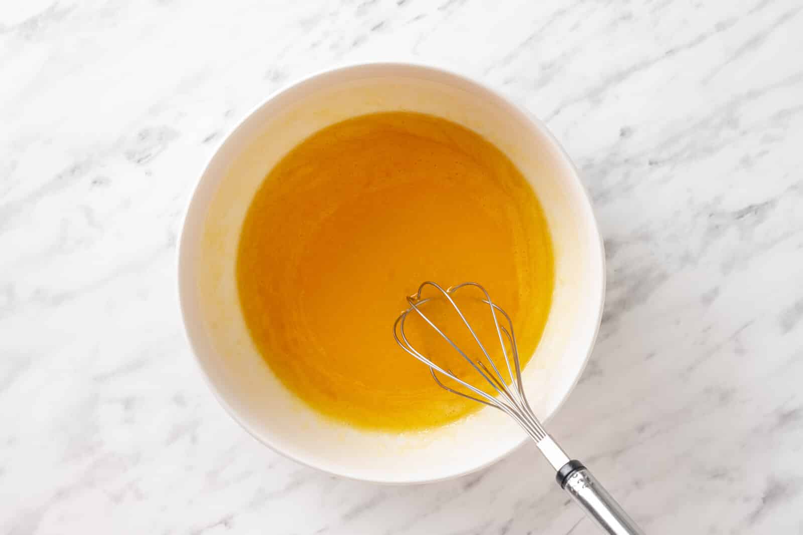 Wet ingredients in a white bowl with a whisk.