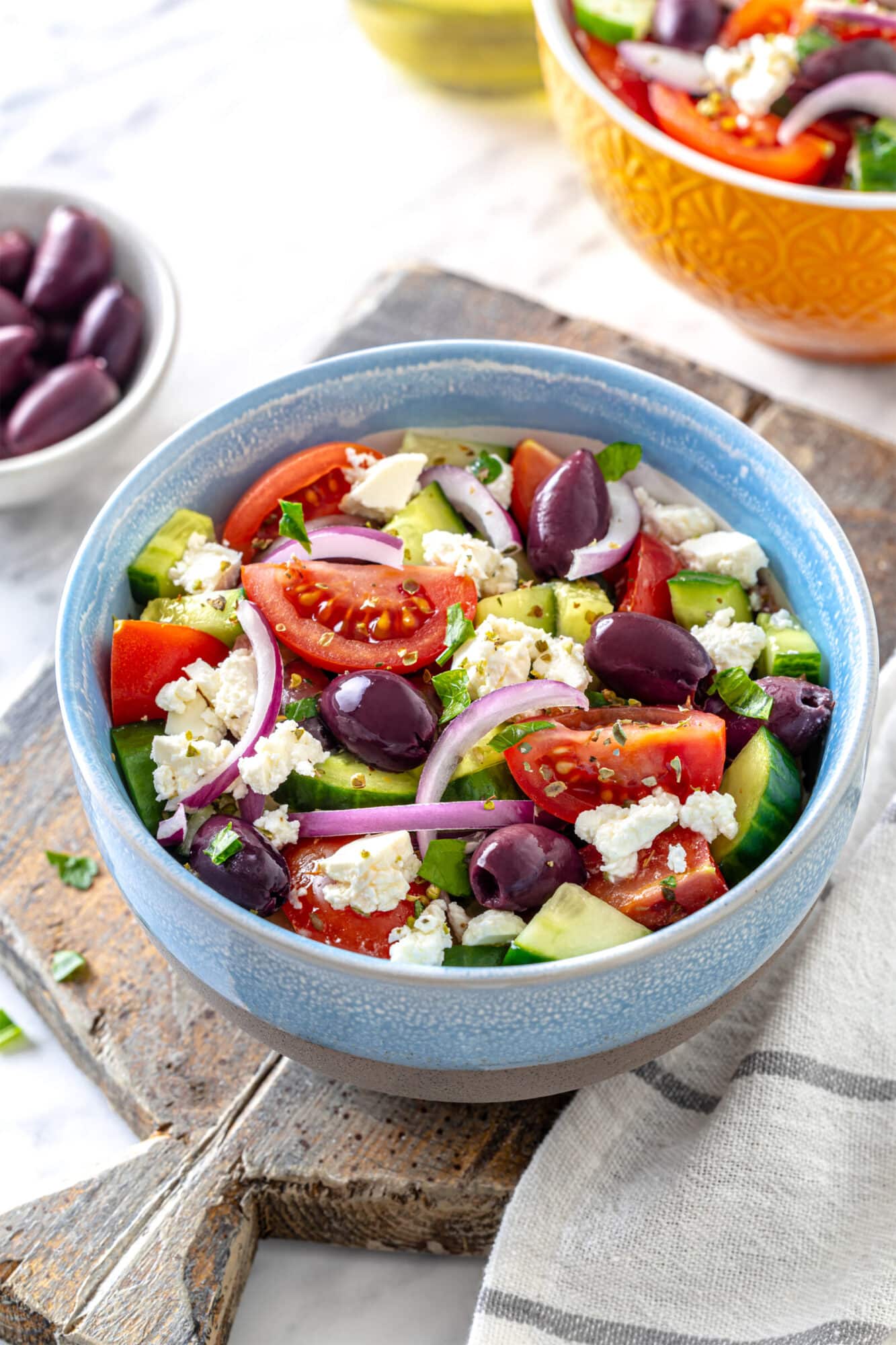 Quick greek salad in a bowl ready to eat, serving on a wooden board with a towel on the side.