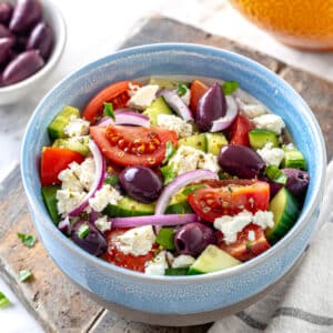 Quick greek salad in a bowl ready to eat, serving on a wooden board with a towel on the side.