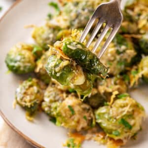 Speared brussels sprout on a fork with more sprouts in the background on a plate.