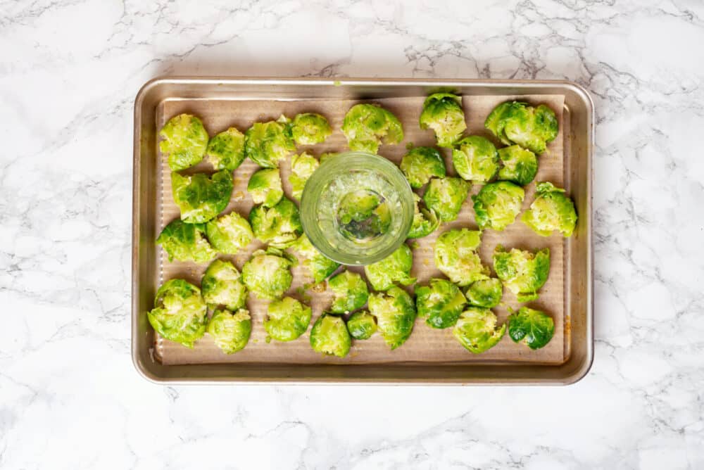 Mashing brussels sprouts with a glass cup.