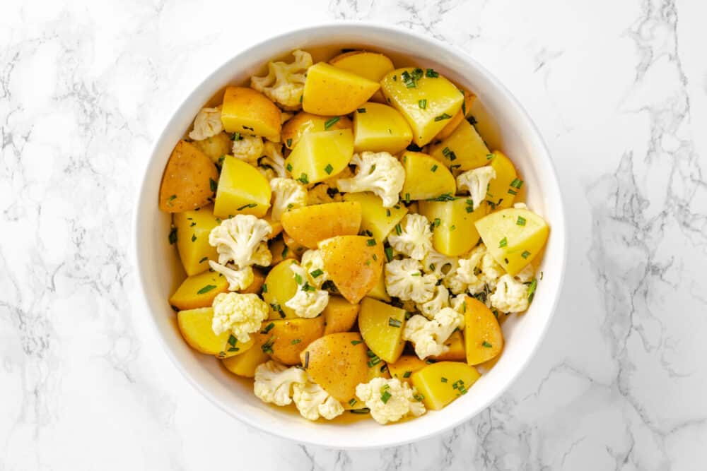 Pre roasted chopped potatoes and cauliflower florets in a bowl.