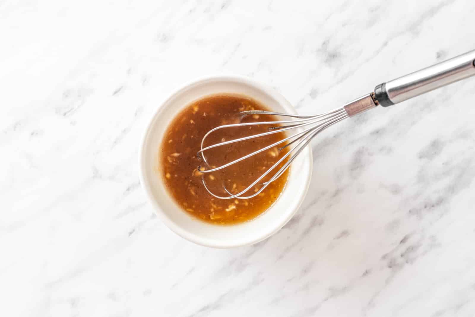 Salad dressing in a white bowl with a whisk.