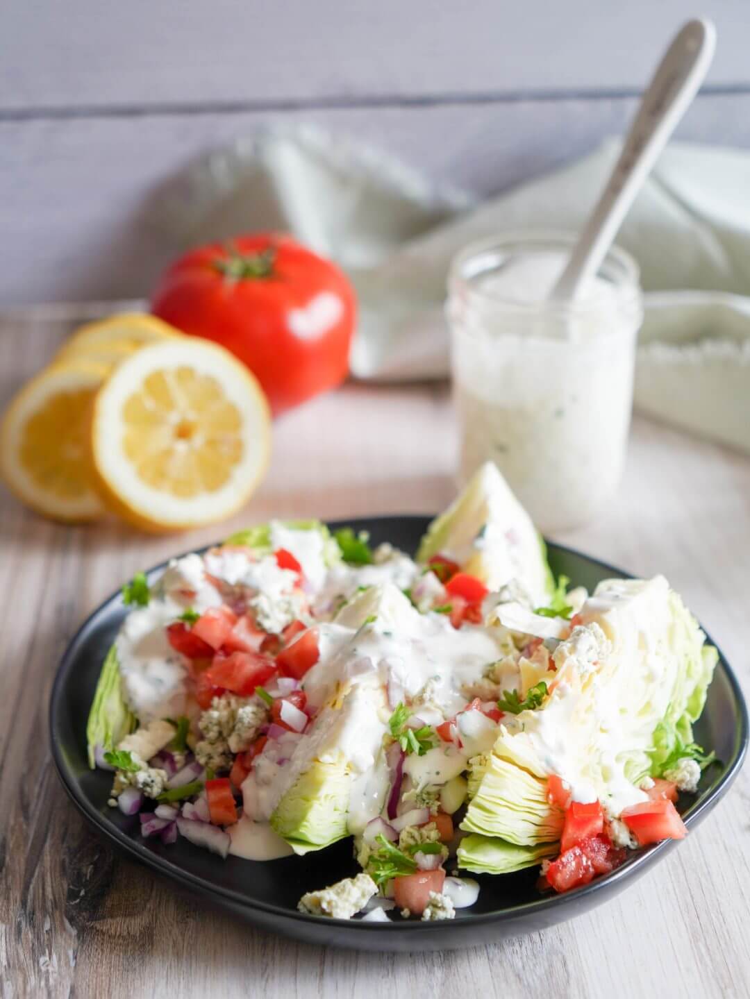 wedge-salad-on-a-black-plate-with-ranch-lemon-and-tomato-in-the-background