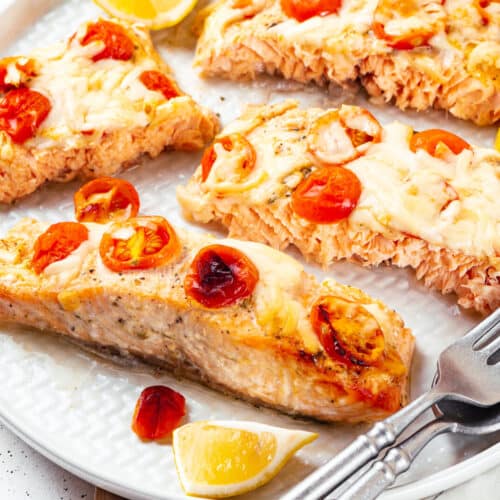 Oven baked salmon slices with lemon wedges for serving atop a plate with forks on the side.