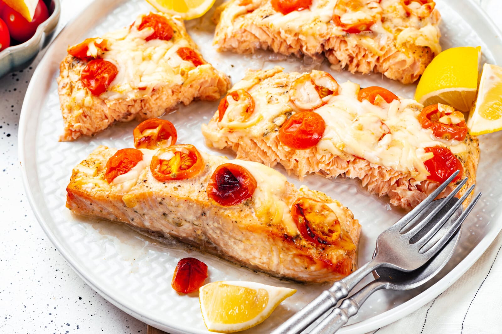 Oven baked salmon slices with lemon wedges for serving atop a plate with forks on the side.