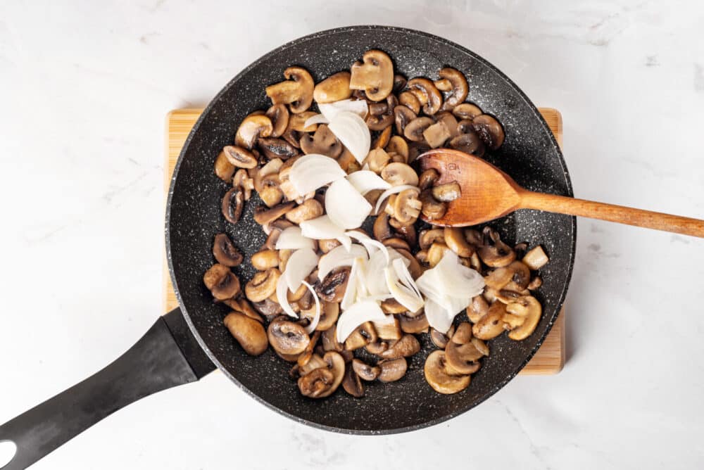 Sautéing onions and mushrooms in a skillet with a wooden spoon