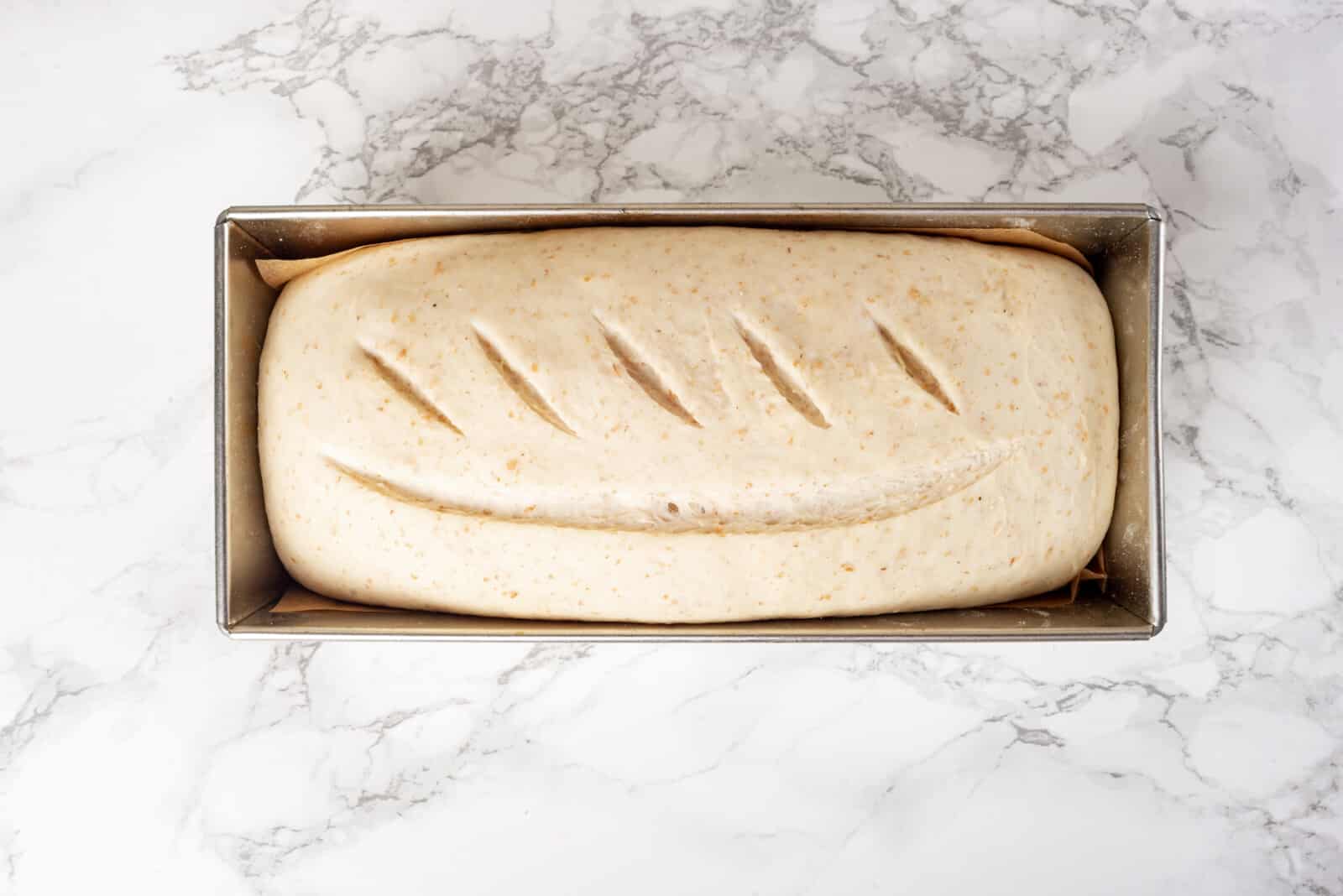 Scored loaf of bread dough ready to bake in a loaf pan.