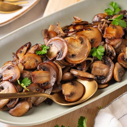 Serving sautéed mushrooms on a white plate with leaves of parsley.