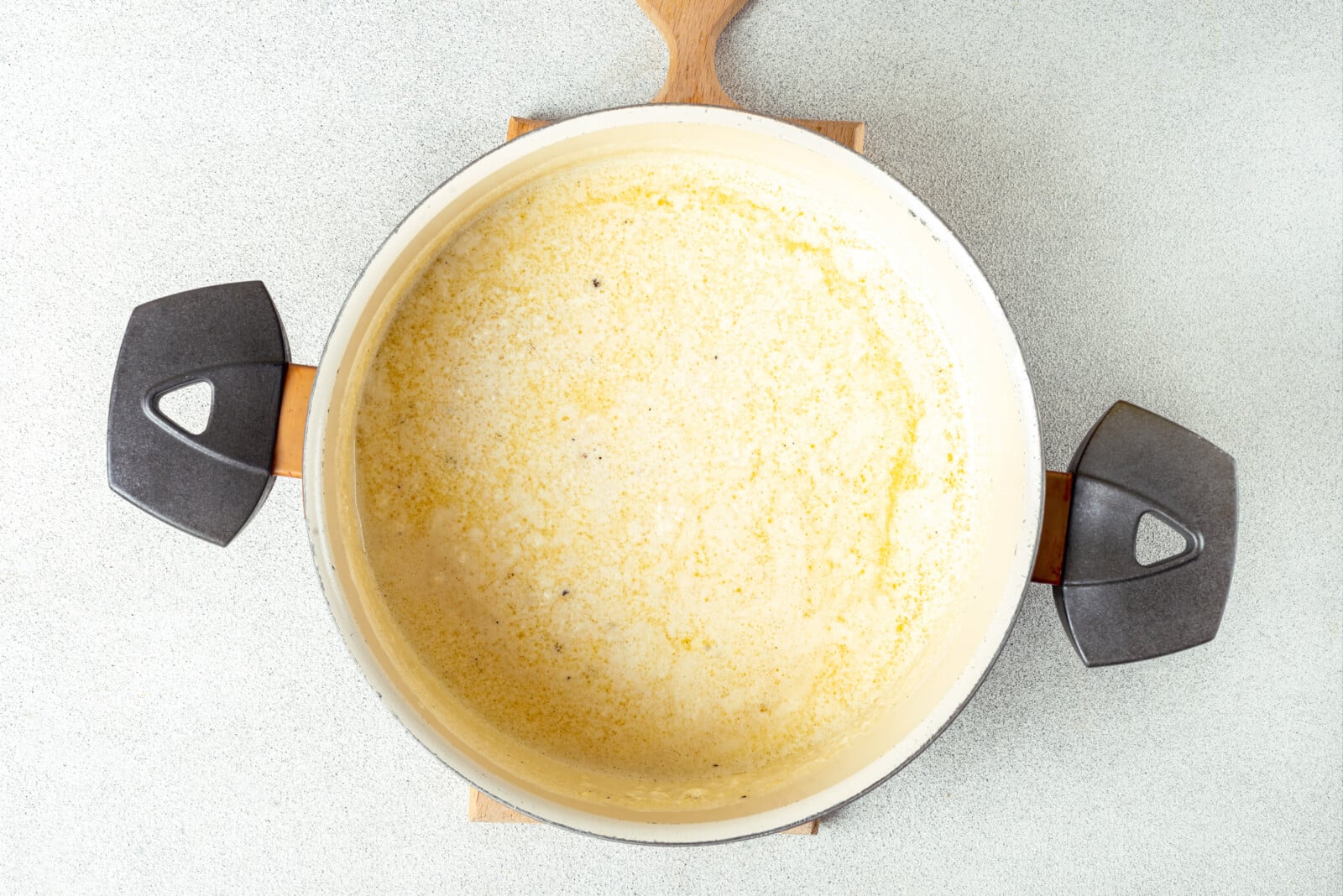 Simmering and melting cheese in a pot with alfredo sauce.