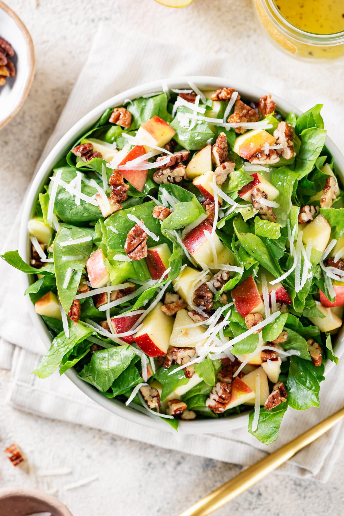 apple chopped with chopped green lettuce shredded cheese and pecans in a white bowl on white towel.