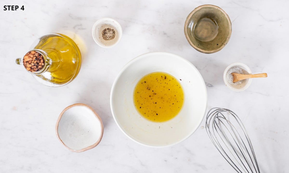 white wine vinegar dressing mix in a white bowl with whisk on the side salt and pepper. 