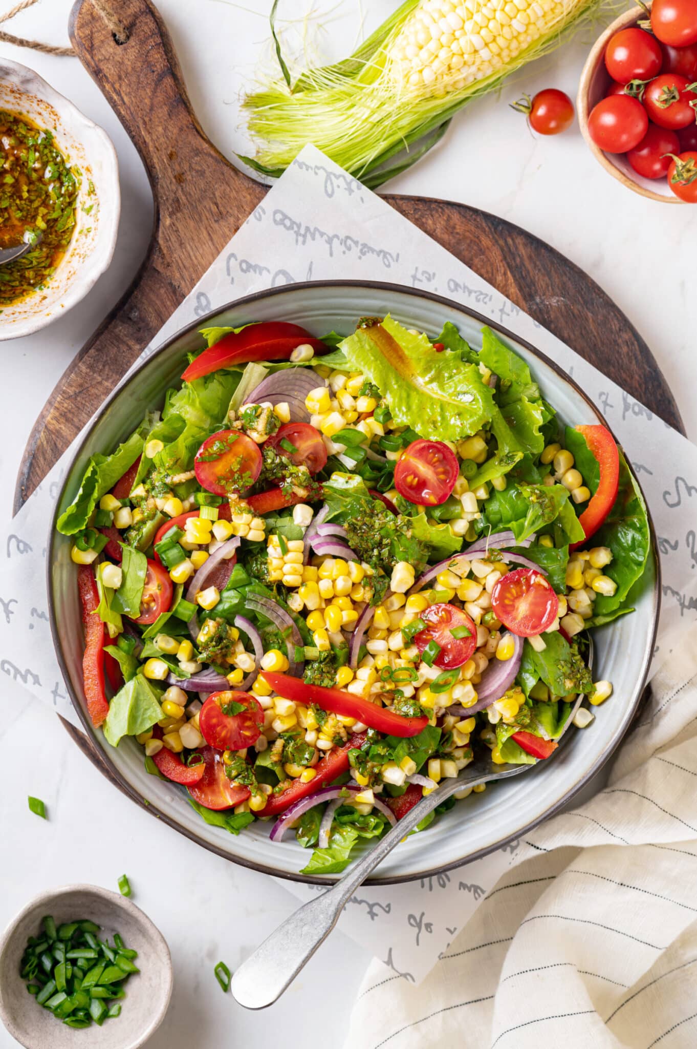 Smoked corn salad in a large bowl displayed atop a wooden cutting board with a spoon for serving.