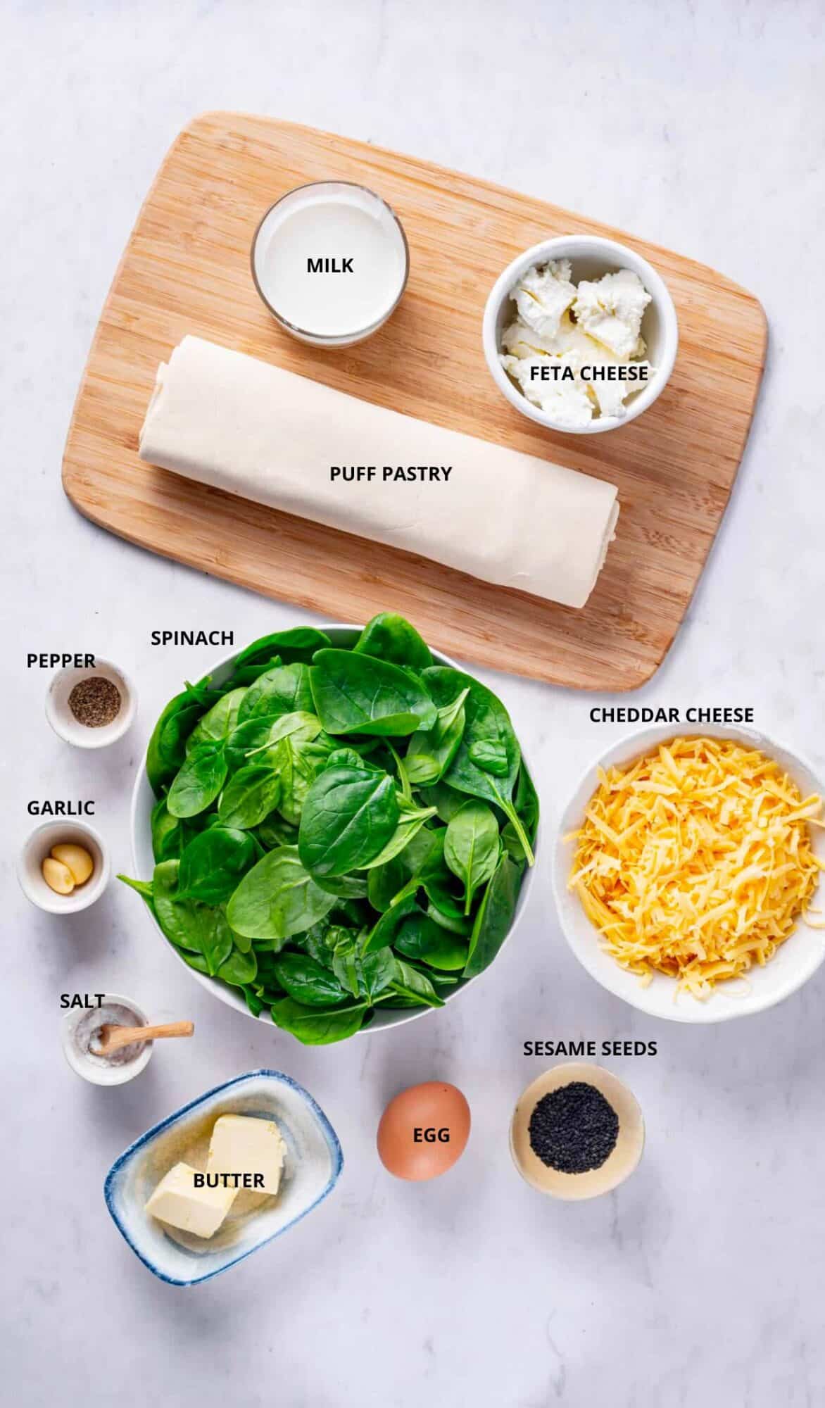 spinach puffs ingredients with labels milk feta cheese puff pastry cheddar cheese spinach pepper garlic salt butter egg and sesame seeds.