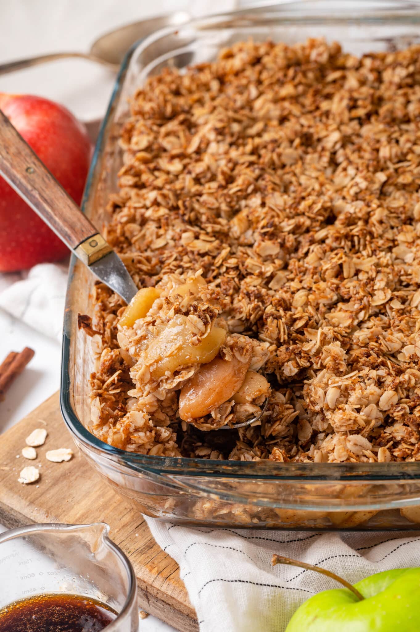 Spooning baked apple crisp from a glass baking dish.